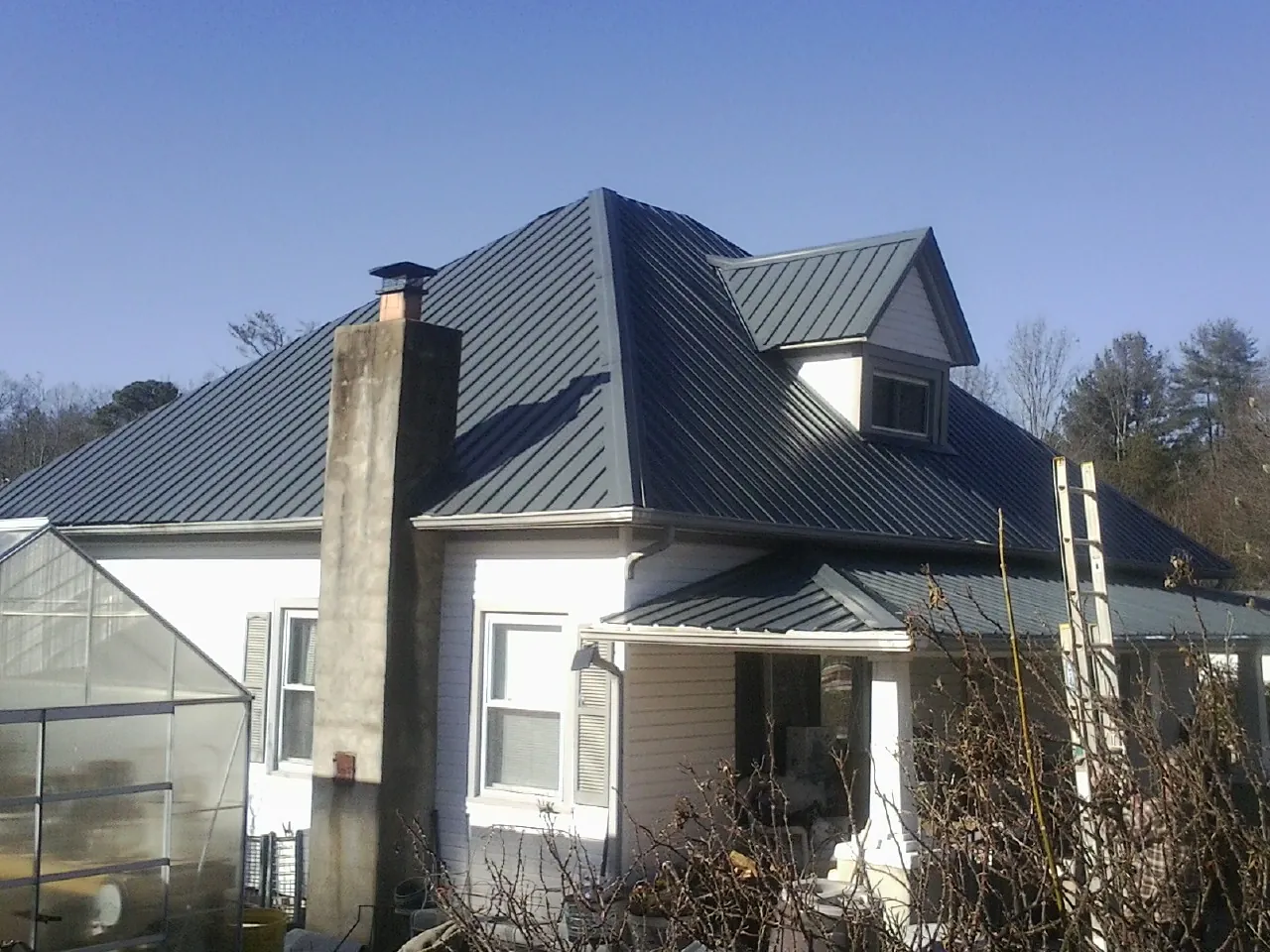 Dark blue standing seam metal roof on a white farmhouse with dormer — Slate & Tile Roof Repair by Roofing Brothers in Dunstable