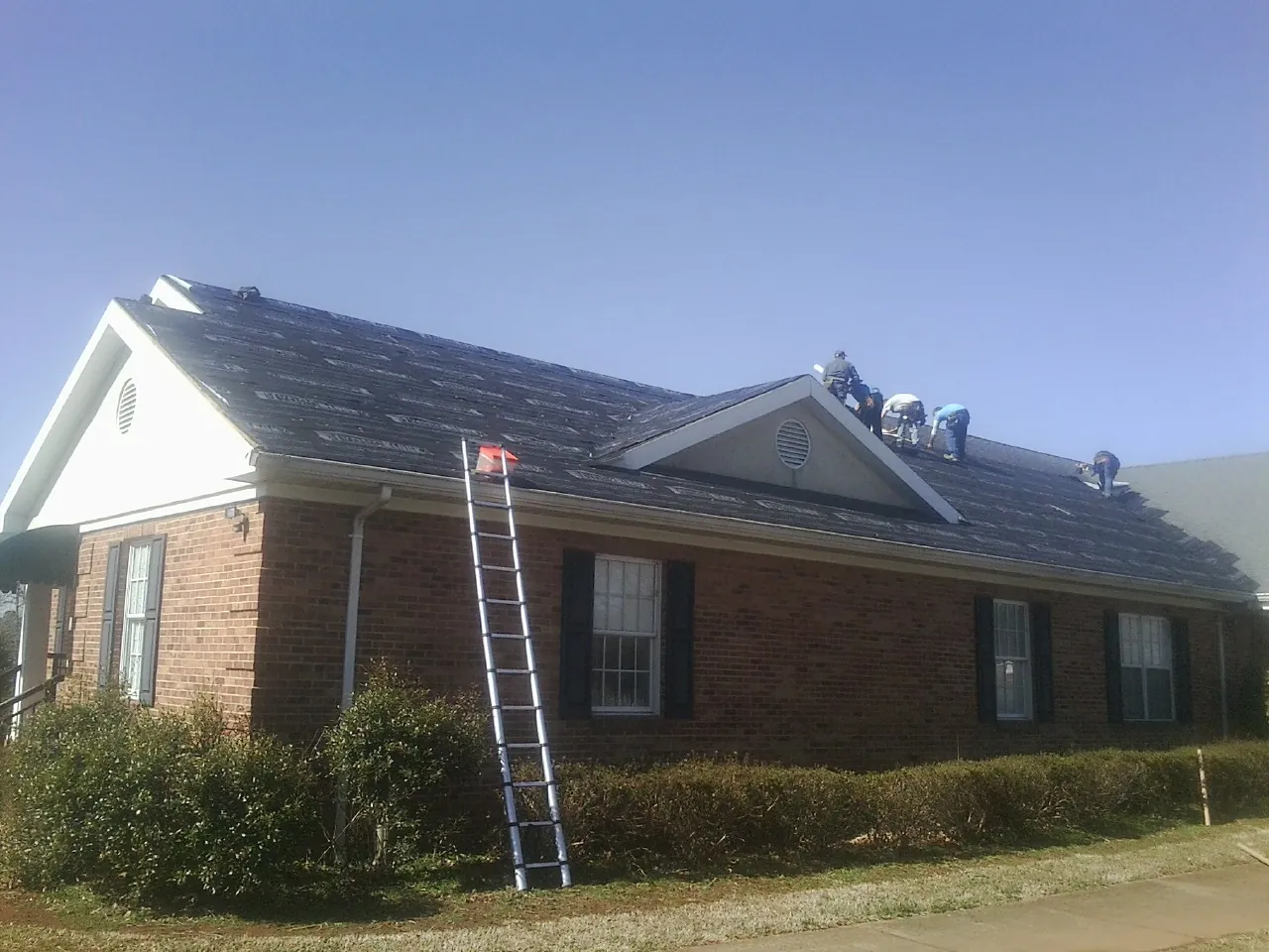 Crew tearing shingles off a brick ranch roof with a ladder set — Emergency Roof Repair work by our crew in Dunstable