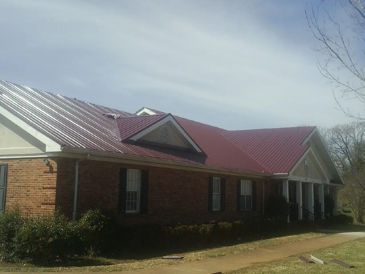 Red metal roof with gabled entries on a long brick building, from a Hail Damage Roof Repair job in Dunstable