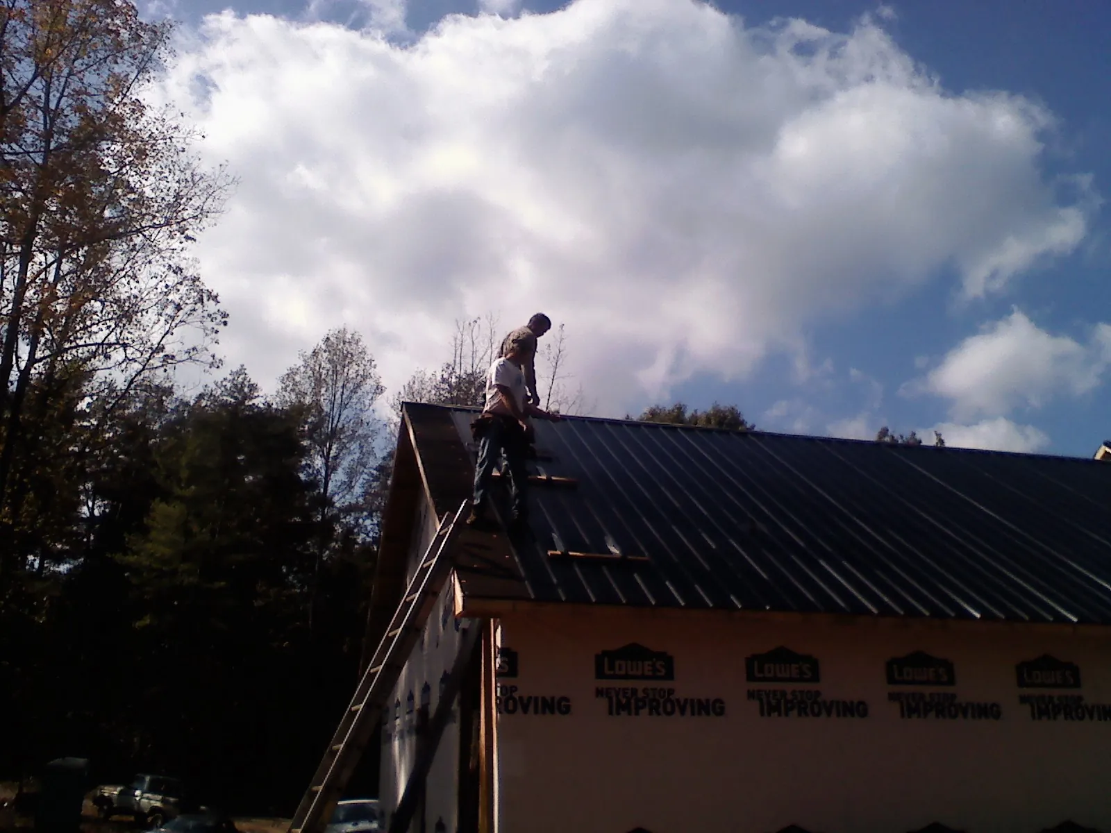 Roofer fastening dark metal panels high against a cloudy sky, from a Roof Inspection job in Dunstable