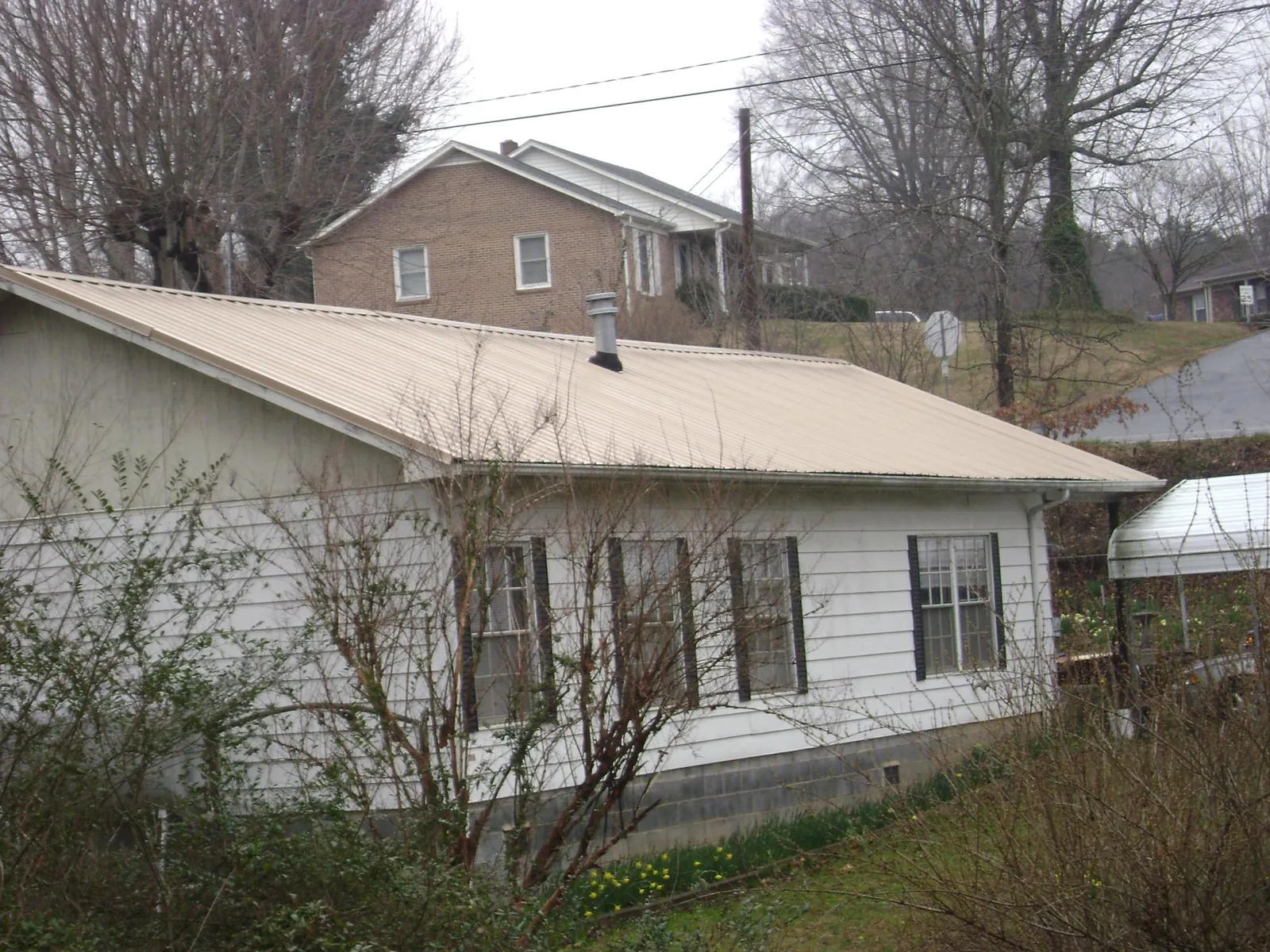 Tan metal roof on a white sided house set into a hillside — Commercial Roofing by Roofing Brothers in Dunstable